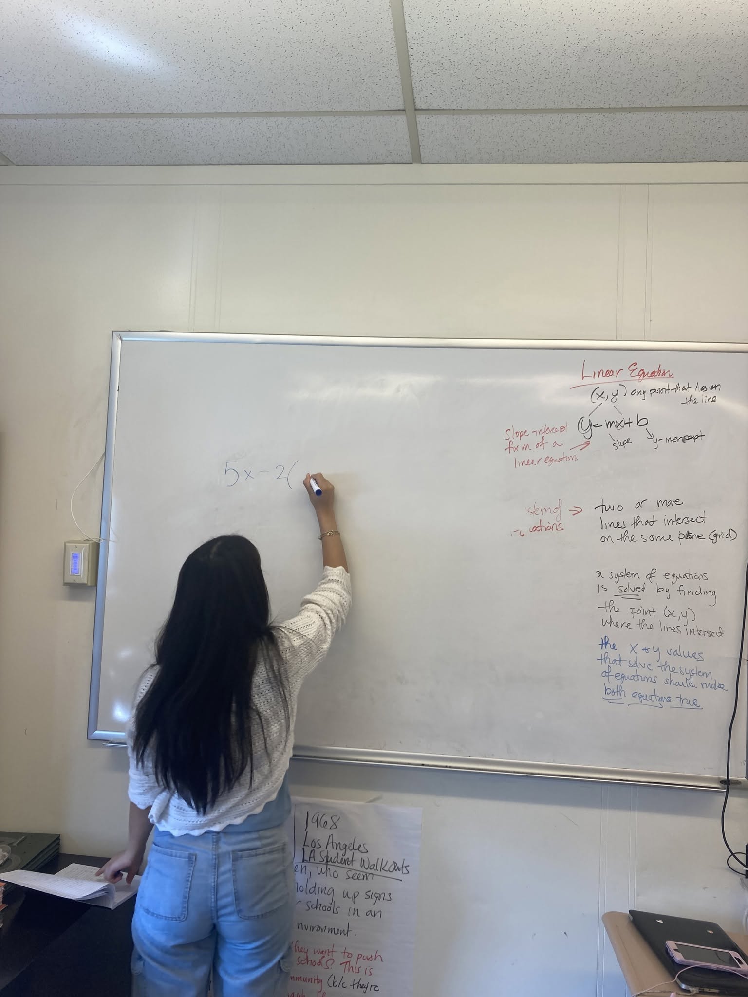 Student writing on whiteboard Student in white top and blue jeans with long black hair writing on a whiteboard with a marker