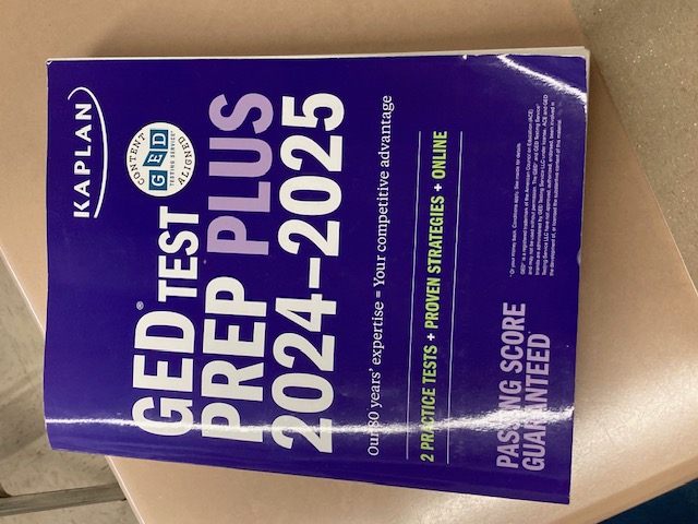 GED Prep Textbook cover Kaplan GED Test Prep Plus 2024-2025 textbook on a desk