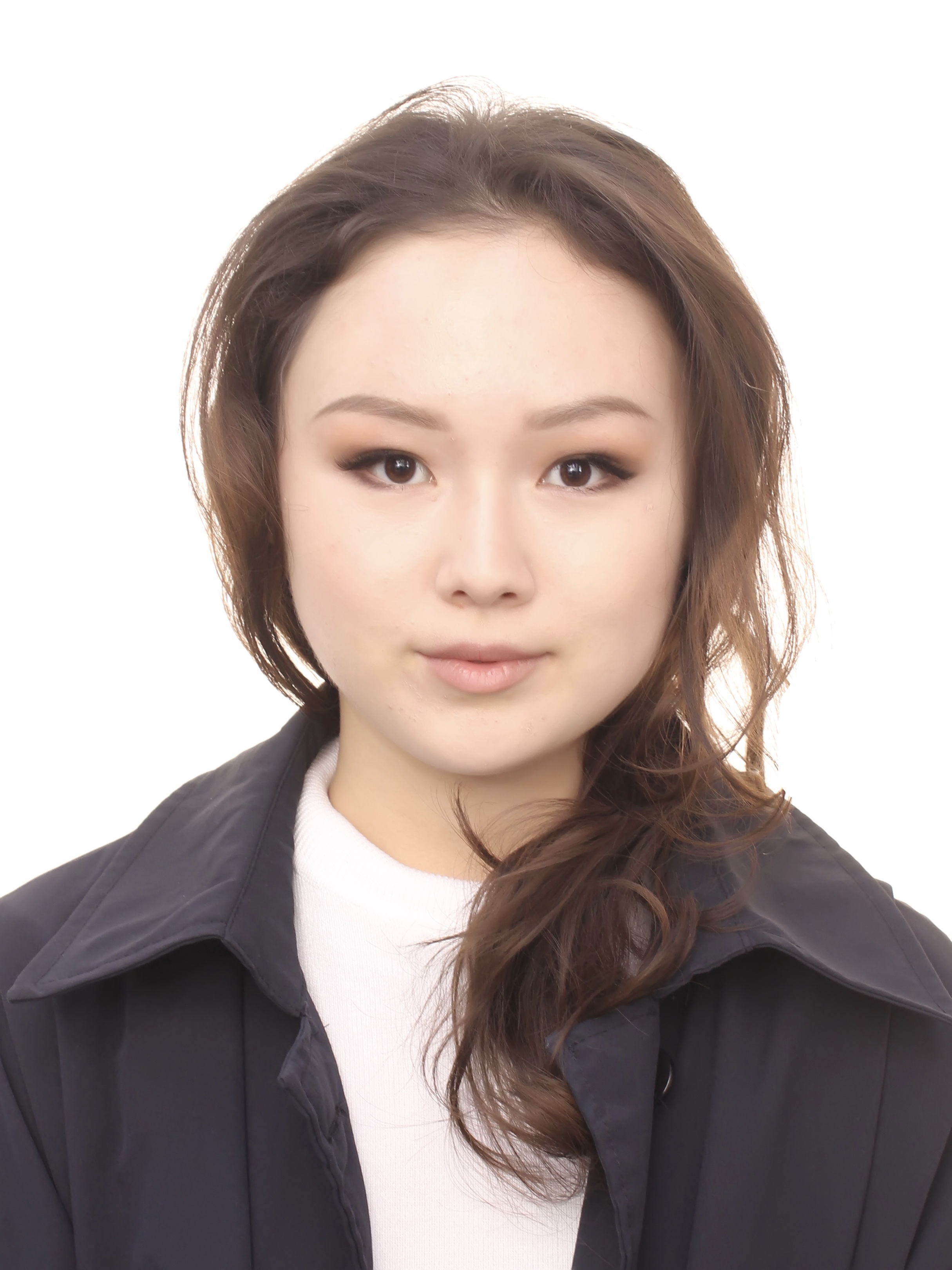 Young woman with long, dark hair over one shoulder wearing a black coat and white shirt against a white wall