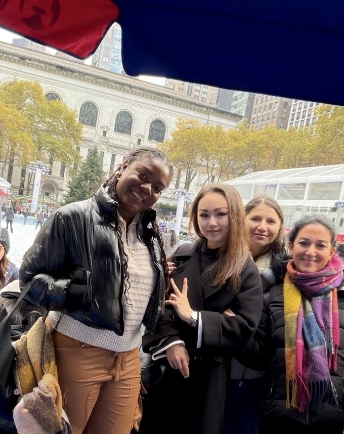 Four female students outdoors in Bryant Park smiling at the camera