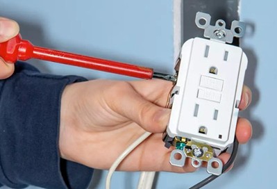 Hands holding an electrical outlet and an insulated screwdriver.