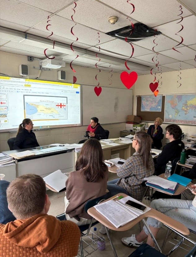 Students in a classroom facing the instructor with class materials projeced onto the whiteboard.