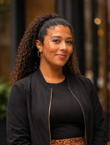 Smiling woman with long curly hair, black jacket and top.