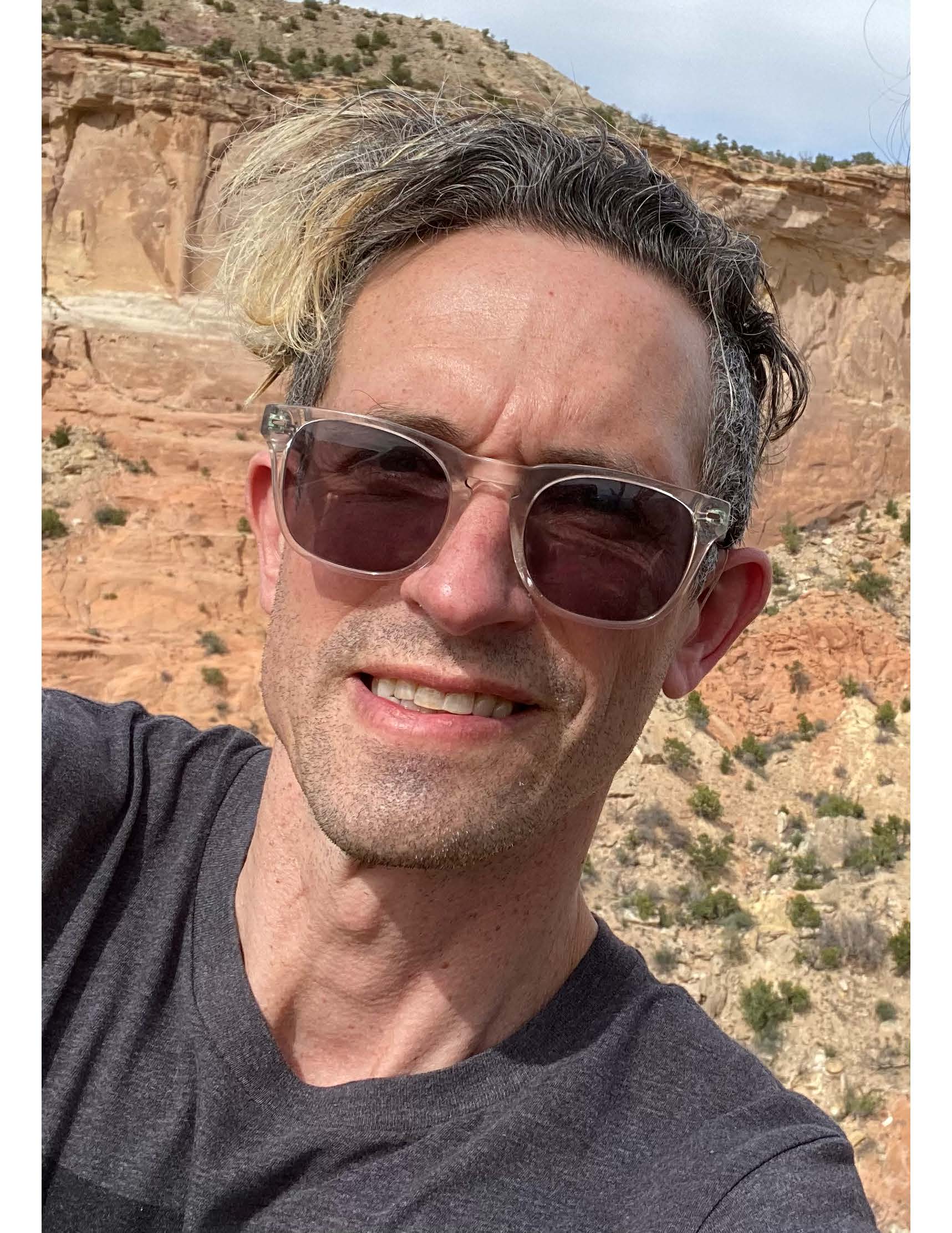 Ryan Chaney Man in sunglasses and grey t-shirt outside in a desert-type setting