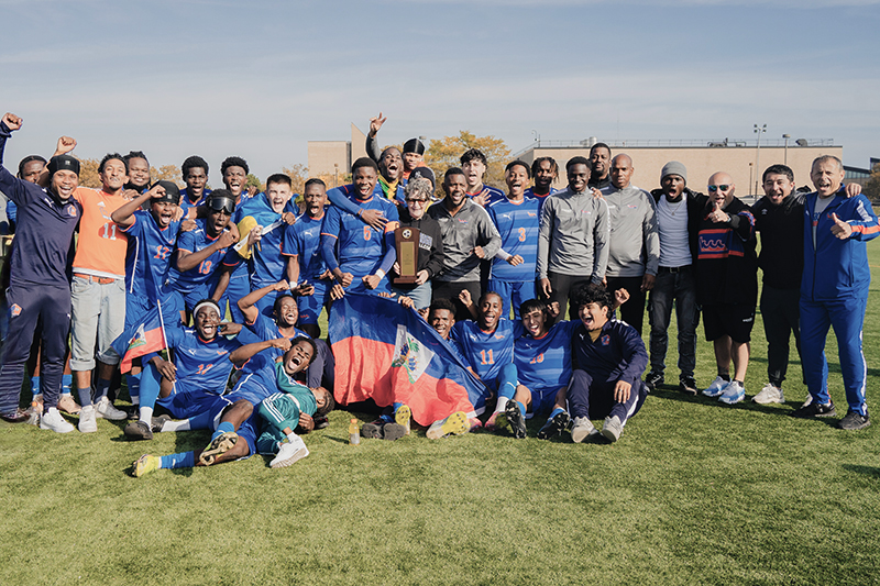 The 2025 Wave roster and coaching sta5 celebrate with Kingsborough President, Suri Duitch following 4-0 win over BMCC in the NYC CC Championship game. 10/19/25 Photographed: IG @ShotsByAyo